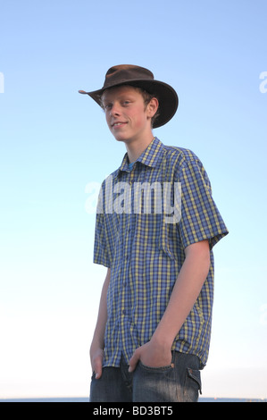 Lächelnde Teenager mit einem Aussie Hut am Strand an einem Sommerabend bei Sonnenuntergang. Stockfoto