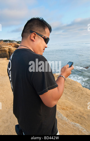 Mann mit seinem iPhone auf einer Klippe über dem Meer. Stockfoto