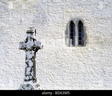 Keltisches Kreuz auf einem Grab im Vordergrund mit einem Kathedrale Fenster im Hintergrund an der Kirche in Kilfenora Irland. Stockfoto