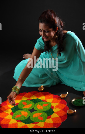 erhöhte Ansicht einer jungen Frau, die Verzierung Rangoli mit Öllampen Stockfoto