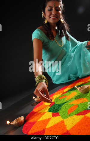 erhöhte Ansicht einer jungen Frau, die Verzierung Rangoli mit Öllampen Stockfoto