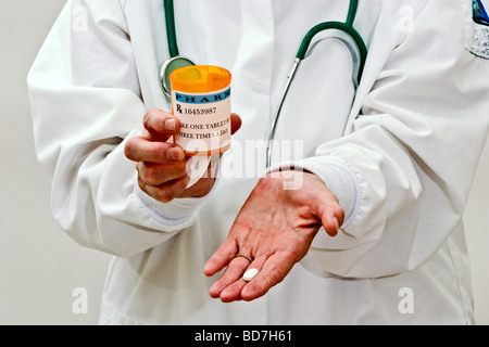 Eine Frau in eine Ärzte Kittel halten einzelne weiße Pille in der Hand und eine Verschreibung Flasche in der anderen Hand mit einem Stethoskop Stockfoto