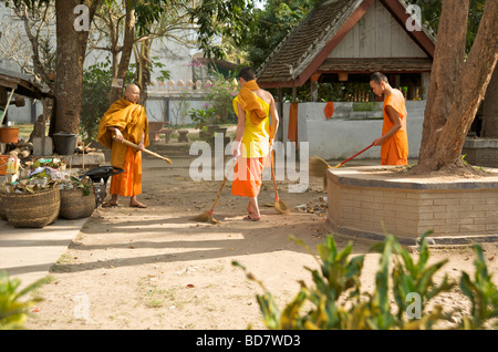 Drei buddhistische Anfänger-Mönche fegen Blätter auf dem Gelände ihres Tempels in Luang Prabang Laos auf Stockfoto