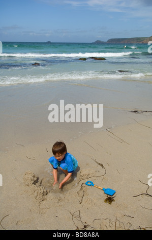 Ein sechs Jahre alter Junge in einem Pinienhain spielt in den Sand am Strand von Sennen Cove, Cornwall, UK Stockfoto