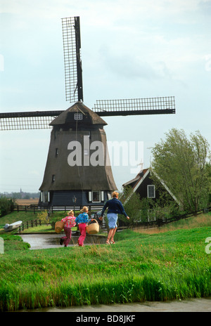 Mutter und Kinder mit Körben zu Fuß nach Hause Weg in Holland in der Nähe von Windmühle und Kanal Stockfoto