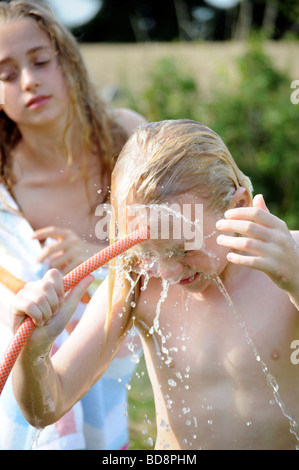 Foto von einem Mädchen waschen und kühlen mit Schlauch-Rohr-Wasser an einem Sommertag im britischen Königreich Garten Stockfoto