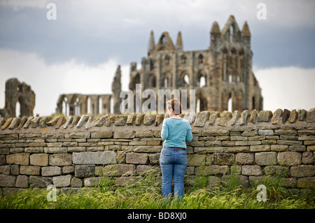 Touristen auf der Suche über eine Mauer in Richtung Whitby Abbey, North Yorkshire, UK. Stockfoto