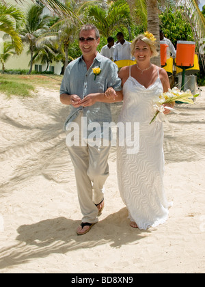 Eine Braut und ihr Vater gehen Arm in Arm auf einem tropischen Strand für ihre Hochzeit Stockfoto