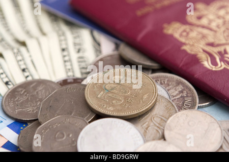 Vorbereitung für einen ausländischen Urlaub: Münzen aus verschiedenen Ländern sind neben einem britischen EU-Pass und US-Dollarnoten angelegt. Stockfoto