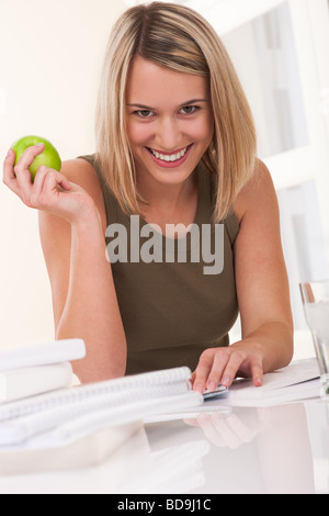 Lächelnde junge Frau am weißen Tisch sitzt und hält Apfel Stockfoto