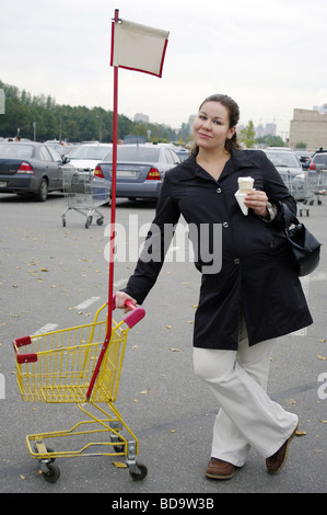 Schwangere Frau bleibt auf dem Supermarkt Parkplatz mit Einkaufswagen sie Eis essen Stockfoto