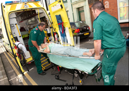 2 Sanitäter, die Beantwortung von ein 999 anrufen setzen ältere Dame, die zu Hause auf einer Bahre in gefallen hat und ihr ins Krankenhaus Stockfoto