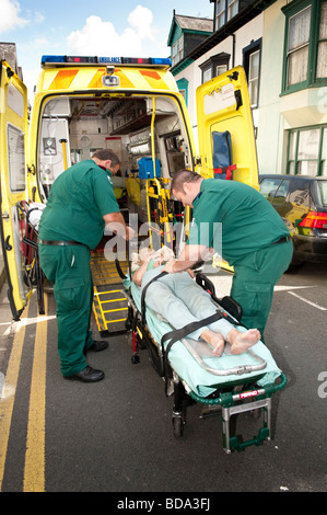 Sanitäter, die Beantwortung von ein 999 anrufen setzen ältere Dame, die zu Hause auf einer Bahre in gefallen hat und ihr ins Krankenhaus Stockfoto