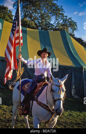 Junge Frau auf weißem Pferd trägt amerikanische Fahne bei der Eröffnungsfeier der Kirmes rodeo Stockfoto