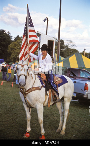 Junge Frau auf weißem Pferd trägt amerikanische Fahne bei der Eröffnungsfeier der Kirmes rodeo Stockfoto