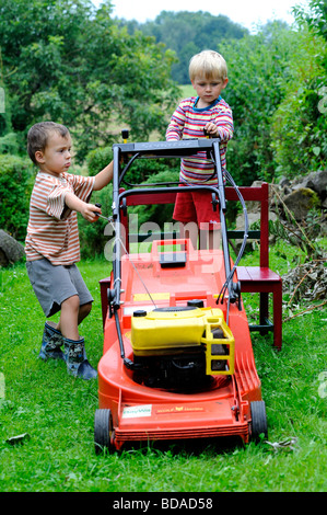 Junge kleine Kinder 2-3-4 Jahre jungen spielen Mäher auf Garten Stockfoto