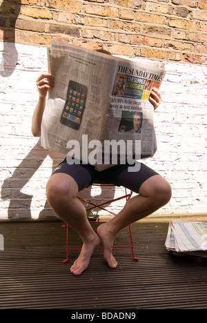 junger Mann in kurzen Hosen sitzen in sonniger Position lesen '' Sunday times'' Broadsheet-Zeitung Stockfoto