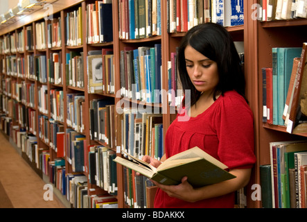 Hispanische junge Frau allein und einem Buch in der Bibliothek Stockfoto
