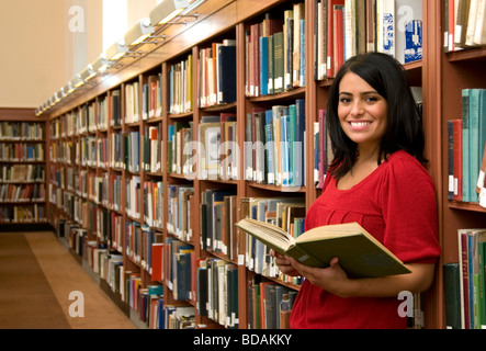 Hispanische junge Frau allein ein Buch hält und lächelnd in der Bibliothek Stockfoto