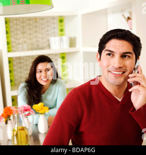 Mitte erwachsener Mann sprechen auf einem Handy mit einer Mitte erwachsenen Frau lächelnd im Hintergrund Stockfoto