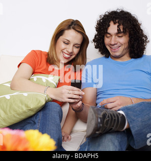 Junges Paar auf einer Couch sitzend und mit Blick auf ein Mobiltelefon Stockfoto