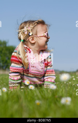 Ein kleines Mädchen mit Blumen im Haar an einem sonnigen Tag in der Wiese liegen. Stockfoto