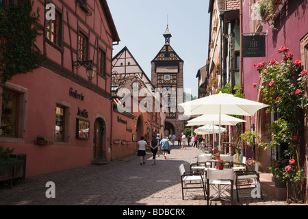 Riquewihr Elsass Frankreich Bürgersteig Café Dolder Turmtor und Altbauten auf schmalen gepflasterten Straße in malerischen mittelalterlichen Stadt Stockfoto