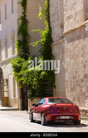 Ein roter Sportwagen in einer Straße in einer kleinen Stadt in Italien geparkt. Alfa Romeo Spinne von hinten in einer Straße in Italien an einem sonnigen Nachmittag gesehen. Stockfoto