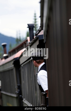 Skagway, Alaska, die Bremse Dirigent auf der White Pass and Yukon Route Railway lehnt sich zwischen Autos für eine bessere Sicht. Stockfoto
