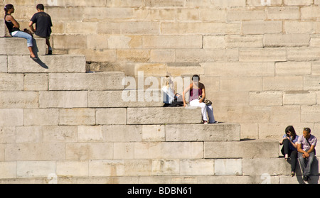 Junge Paare & Menschen genießen die sonnigen entspannen, lesen und sprechen auf den steinernen Stufen an der Seite der Seine, Paris Stockfoto