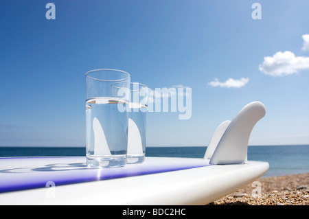 Surfbrett am Strand mit zwei Gläser Wasser Stockfoto