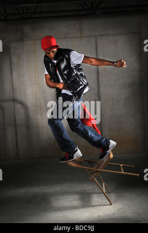 Hip Hop Tänzer Durchführung industrieller Hintergrund auf Stuhl umfallen Stockfoto