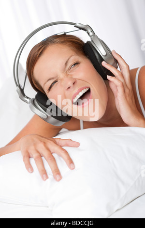 Junge Frau in weiß mit Kopfhörern anhören von Musik im Schlafzimmer und Gesang Stockfoto