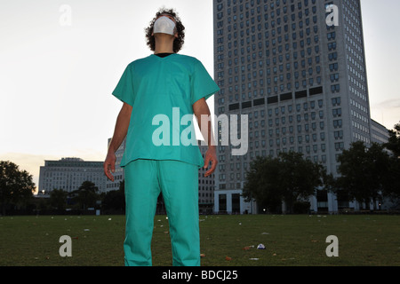 Ein junger Mann mit einem chirurgischen Gesichtsmaske und medizinische Uniform schaut in den Himmel. Stockfoto