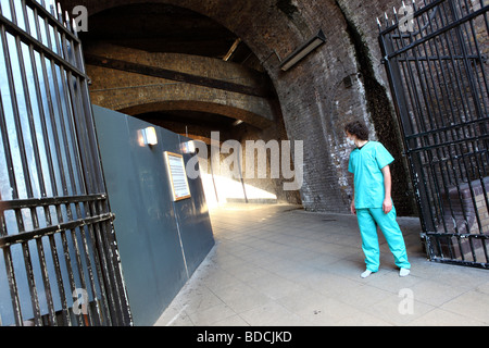 Ein junger Mann mit einem chirurgischen Gesichtsmaske und medizinische Uniform sieht hinter ihm. Er steht auf der Themse Weg in South Bank, London Stockfoto