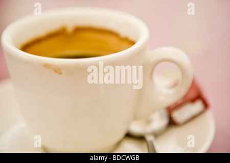 Die Hälfte trank Tasse Espresso in eine weiße Tasse auf einem weißen Teller mit einem Löffel und ein Würfel Zucker Stockfoto