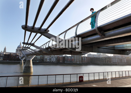 Ein junger Mann mit einem chirurgischen Gesichtsmaske und medizinische Uniform steht immer noch auf die Millenium Fußgängerbrücke, London. Stockfoto