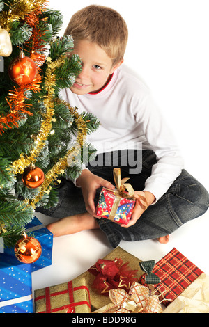 Porträt von fröhlicher Junge hält Weihnachten präsentiert, versteckt sich hinter Weihnachtsbaum Stockfoto