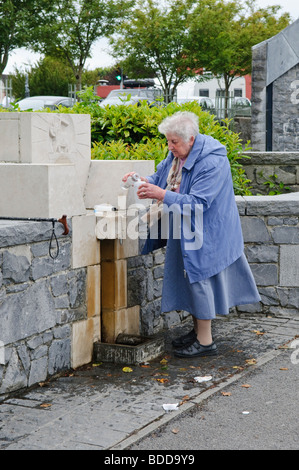 Ältere Frau füllt eine Plastikflasche mit Wasser aus einem Hahn, außerhalb Unserer Lieben Frau von Knock Basilika, Irland Stockfoto