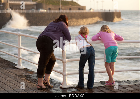 eine Mutter und ihren beiden Töchtern beobachten die Wellen gegen die Promenade, Aberystwyth Wales UK Stockfoto