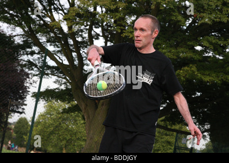 Mann von etwa 40 Jahre alt mit dem Tennisspielen in seinem lokalen park Stockfoto