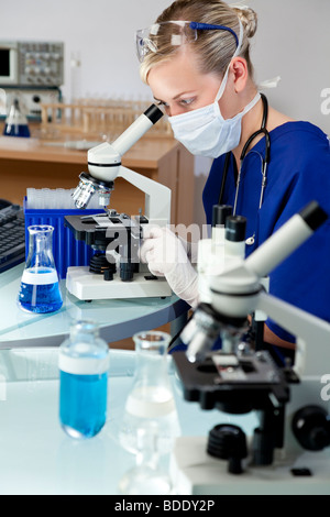 Eine blonde weibliche Ärztin oder wissenschaftlicher Mitarbeiter mit ihrem Mikroskop im Labor. Stockfoto
