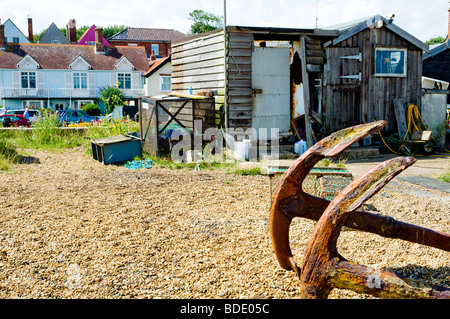 Alte Eisen-Anker in Ruhe und rosten auf dem Kiesstrand; in Aldeburgh, Suffolk, England. Mit baufälligen Hütten als Kulisse. Stockfoto