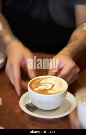 Barista anzeigen und Schaum Kunst in Cappuccino zu dienen.  Nahaufnahme von Händen, Armen mit Tattoos. Stockfoto