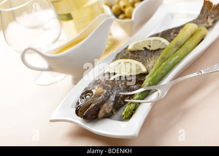 Gebackene Forelle mit Zitrone und Spargel auf einem Tisch mit Weißwein Stockfoto