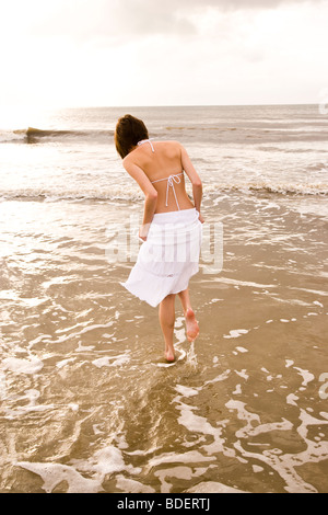 Rückansicht des jungen Frau in Rock und Bikini Top walking im Ozean am Strand Stockfoto