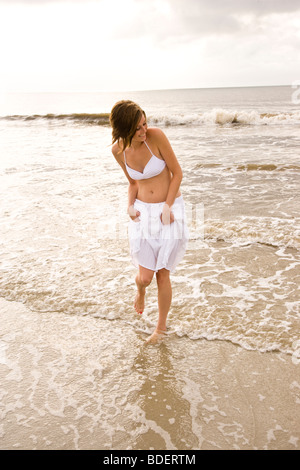 Glückliche Mädchen in weißen Bikini-Oberteil und Rock in der Brandung am Strand zu Fuß Stockfoto