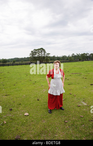 Ältere Frau im roten Kleid und Schürze im grünen Feld Stockfoto