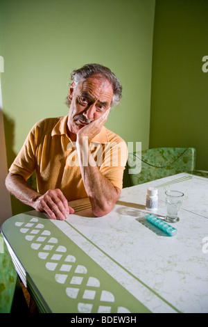 Einsamer älterer Mann sitzt am Küchentisch mit Medizin Pillen Stockfoto