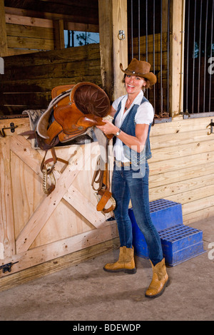 Attraktive Frau mit Sattel im Stall Stockfoto